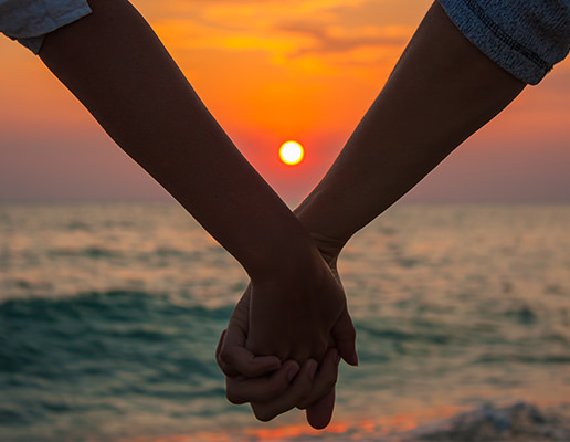Couple holding hands lovingly in front of sunset
